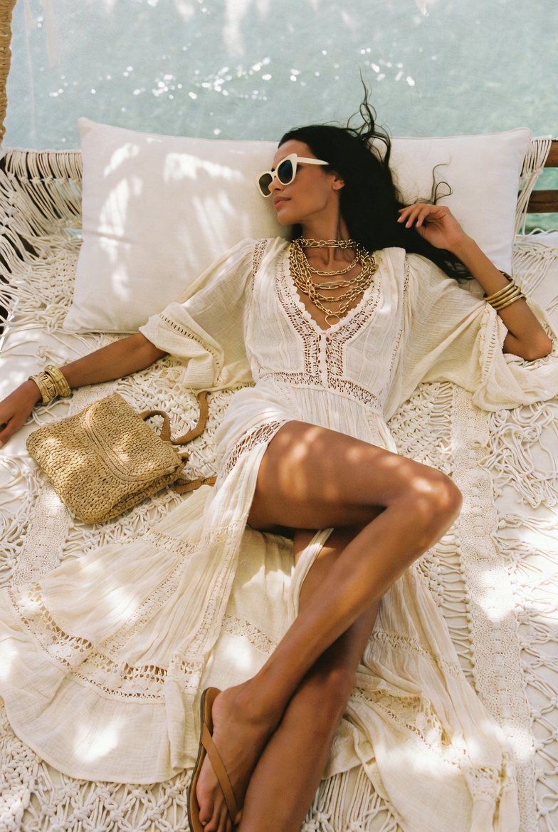A woman reclining on a bohemian daybed in a boho-luxe crochet dress at an Amalfi beach club