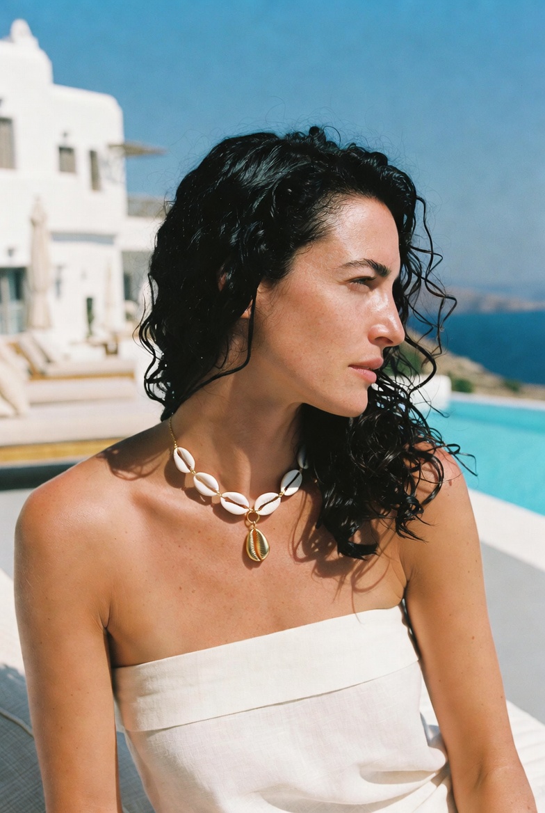 The Shell Necklace — a woman in a white hotel pool in Greece wearing a gilded shell necklace, ESVRA Most Wanted